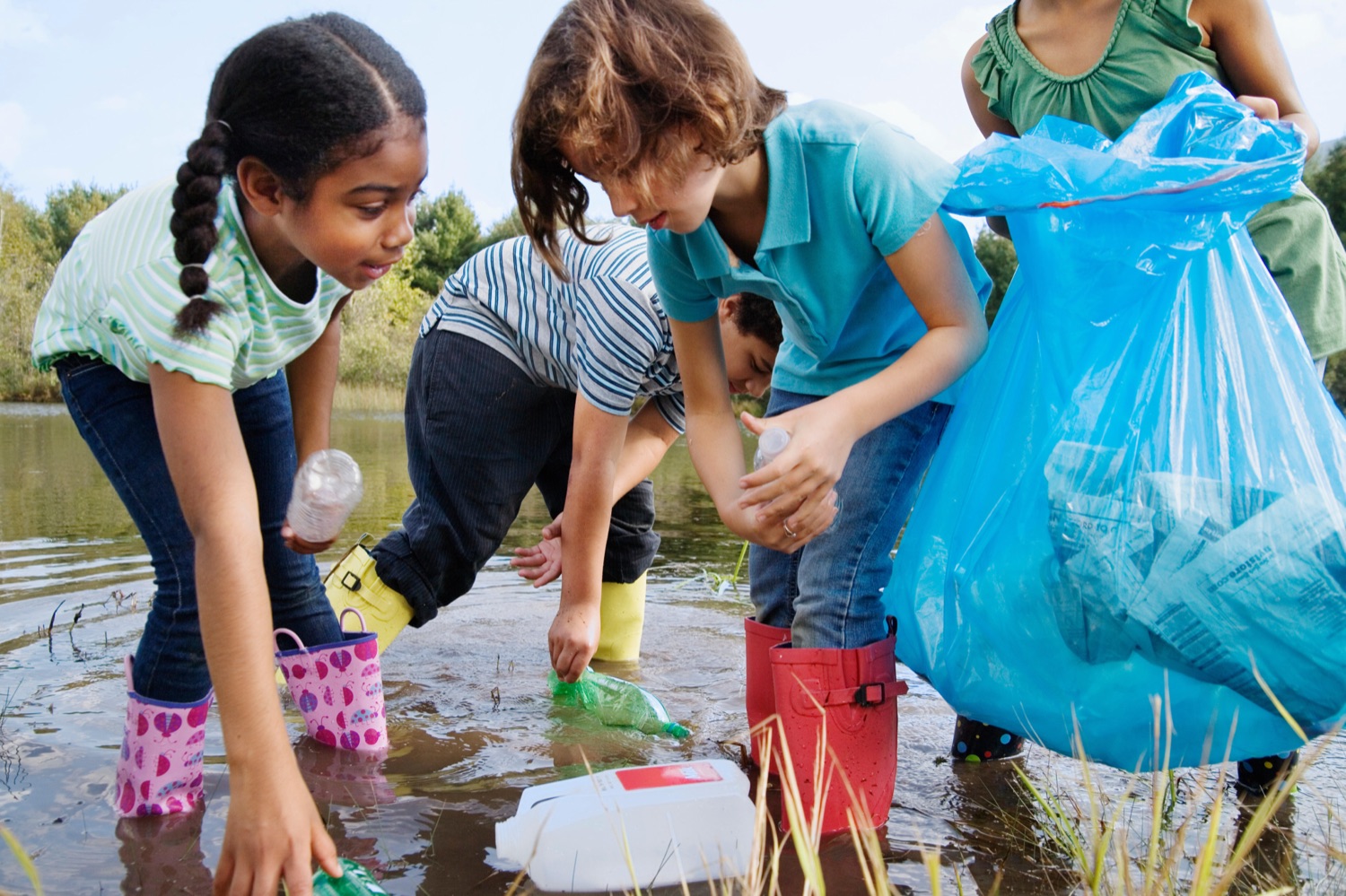Kids in rain boots collecting bottles from a stream during a cleanup