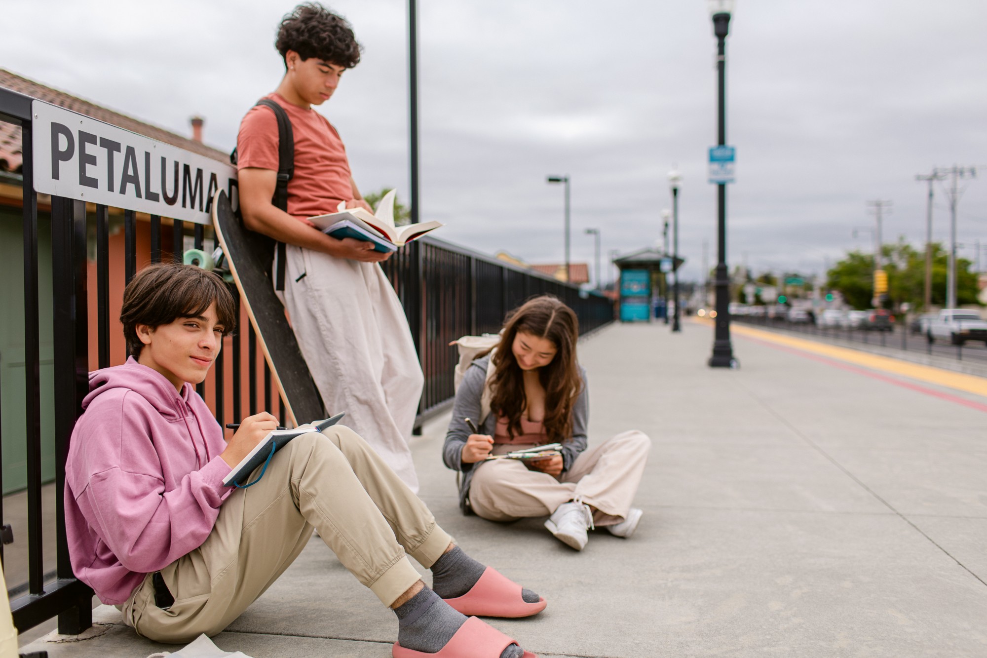 Three teenagers reading and writing on a train platform