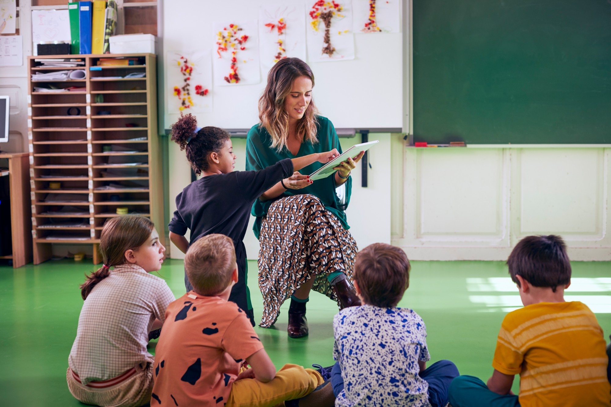 A teacher showing a tablet to children sitting on the classroom floor